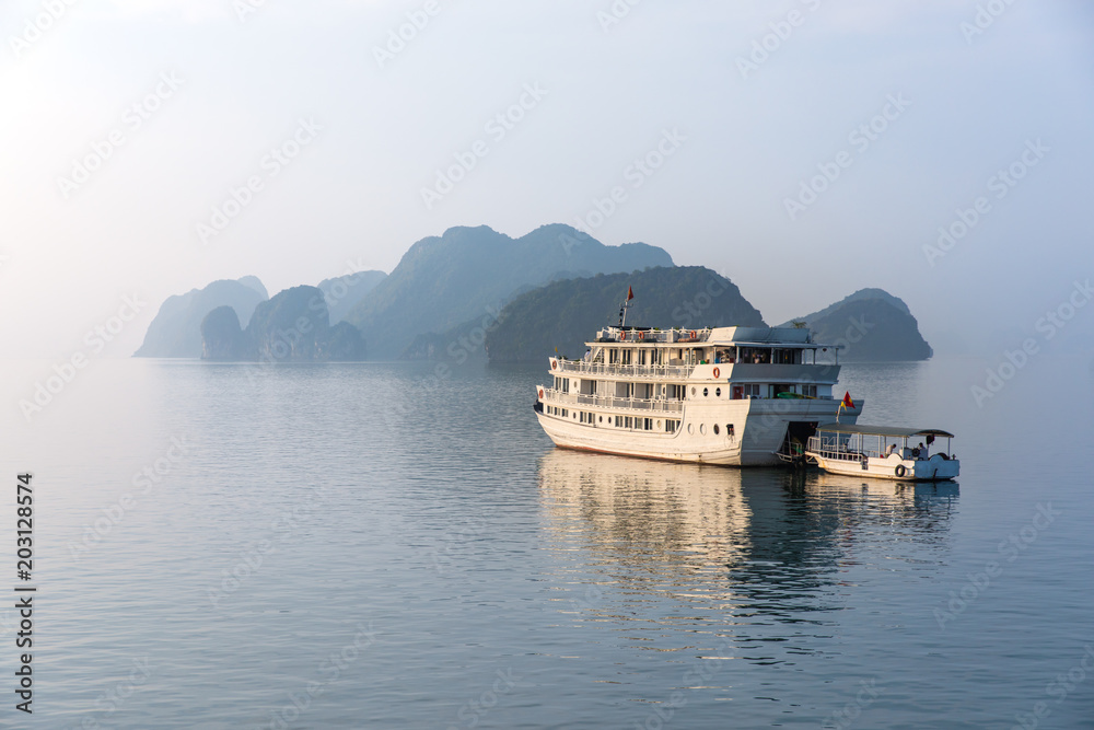 Big tourist cruise boat on the quiet water of Halong Bay (Unesco Heritage site) during late afternoon on the backdrop of a limestone rock mountain. Halong Bay, Vietnam.