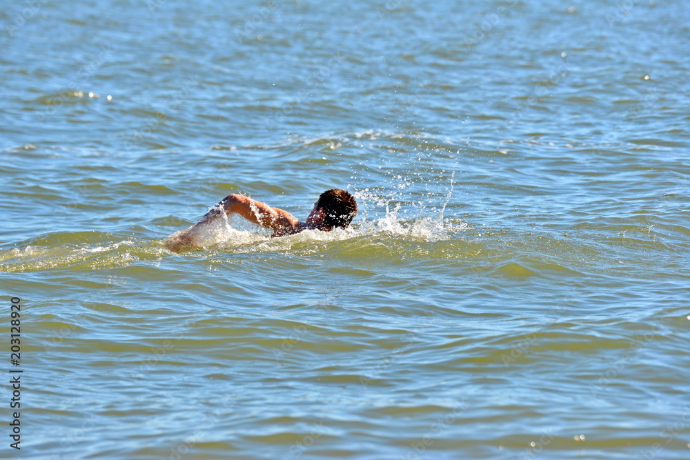 Fototapeta premium A man swims and sinks into the water at sea, goes in for sports for a healthy lifestyle.