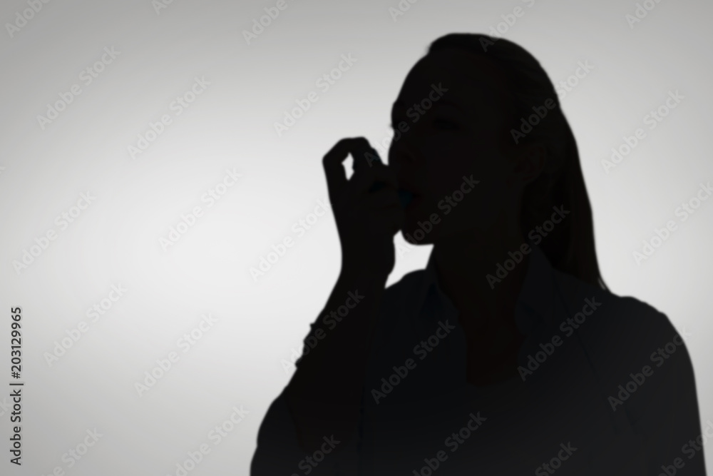 Pretty blonde using an asthma inhaler against grey vignette Pretty blonde using an asthma inhaler against grey vignette