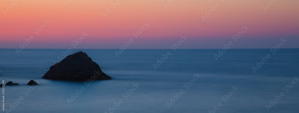 Eine kleiner Felsen im Meer vor Elba in Langzeitbelichtung in blauen und rötlichen Farbtönen