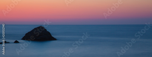 Eine kleiner Felsen im Meer vor Elba in Langzeitbelichtung in blauen und rötlichen Farbtönen