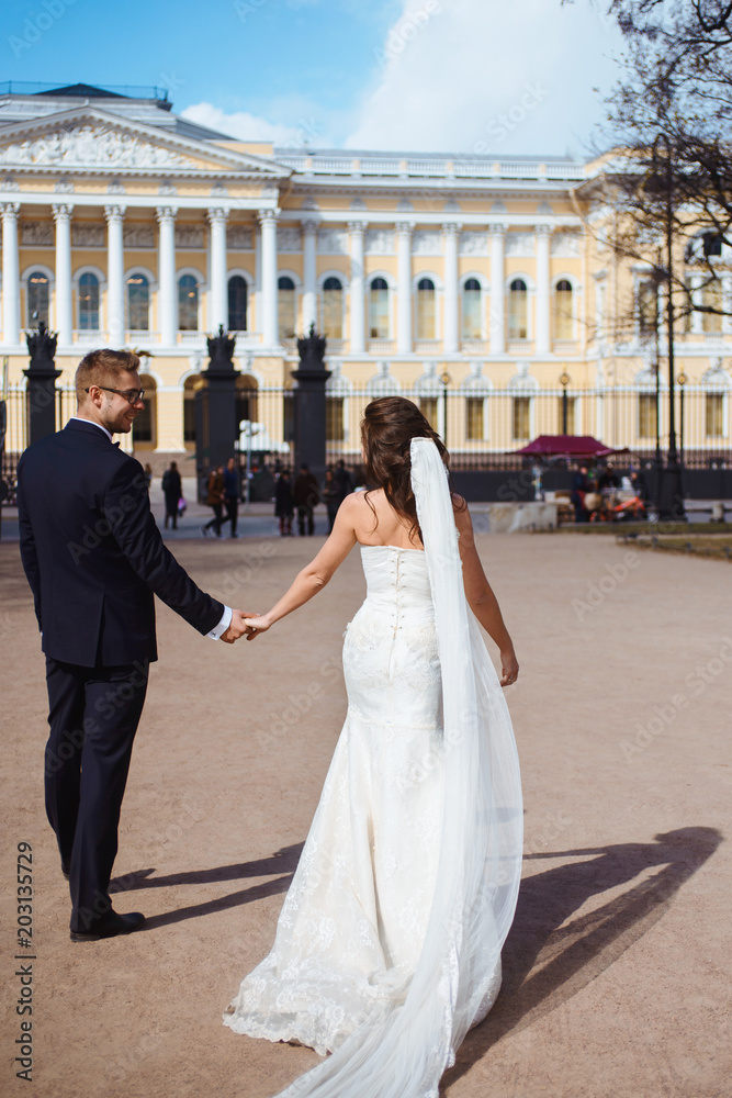 Obraz premium Newlywed couple bride and groom photoshoot after wedding ceremony in Saint-Petersburg Russia. White wedding dress with long veil and classical black suit or smoking with bowtie. Businessman in glasses