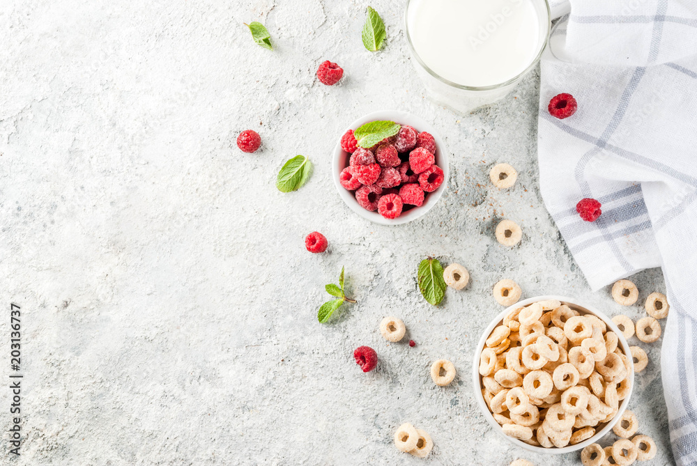Healthy breakfast ingredients. Breakfast cereal corn rings, milk or yogurt glass, raspberries and mint on grey stone background, copy space top view
