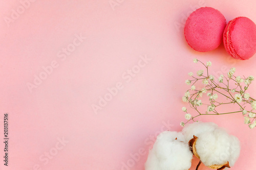 Top view of mini pink macaron or macaroon french desserts cake with cotton flowers on soft sweet pink pastel geometric paper flat lay background.