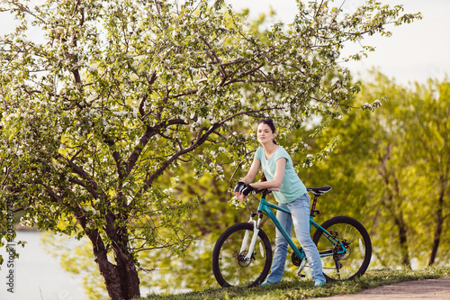 Young woman with bicycle on nature. Blossoming tree in spring