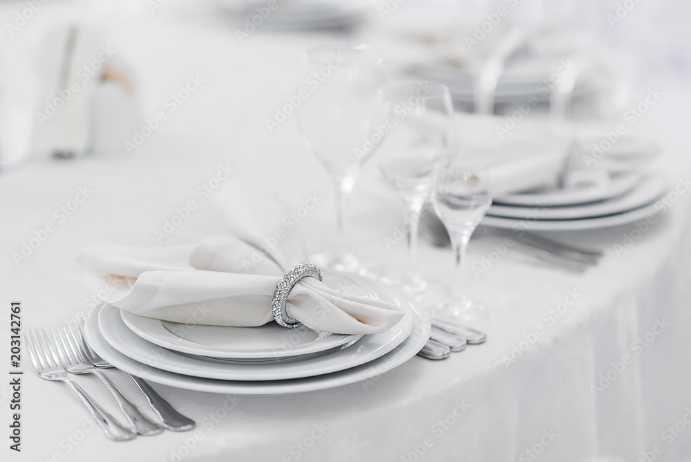 Silver cutlery and stylish white plates are laid out on a white tablecloth of expensive fabric in a restaurant for a festive banquet
