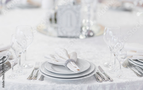 Silver cutlery and stylish white plates are laid out on a white tablecloth of expensive fabric in a restaurant for a festive banquet