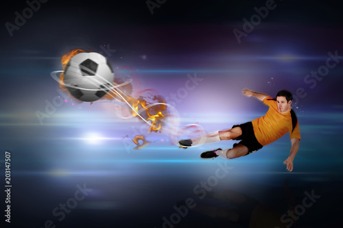 Football player in orange kicking against black background with spark