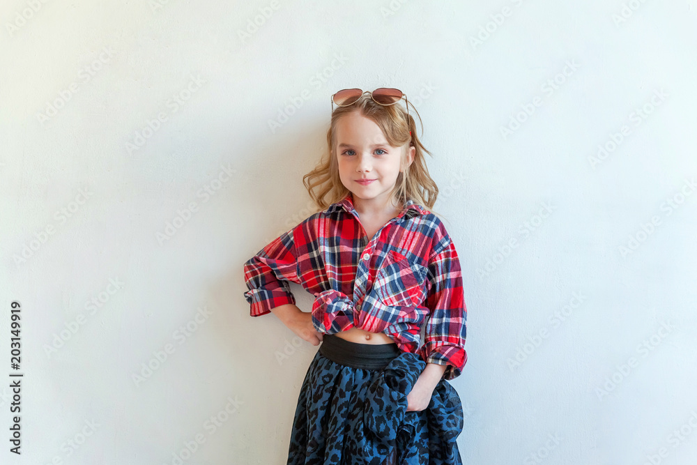 Sweet happy adorable fashion young little girl dressed like hipster hippie gipsy cowboy in sunglasses standing against white wall background in light bright room. Lifestyle people trendy concept Sweet happy adorable fashion young little girl dressed like hipster hippie gipsy cowboy in sunglasses standing against white wall background in light bright room. Lifestyle people trendy concept