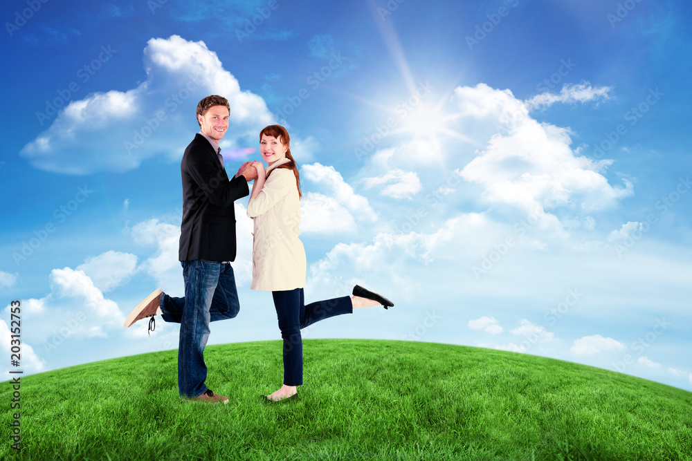 Smiling couple with raised legs against green hill under blue sky Smiling couple with raised legs against green hill under blue sky