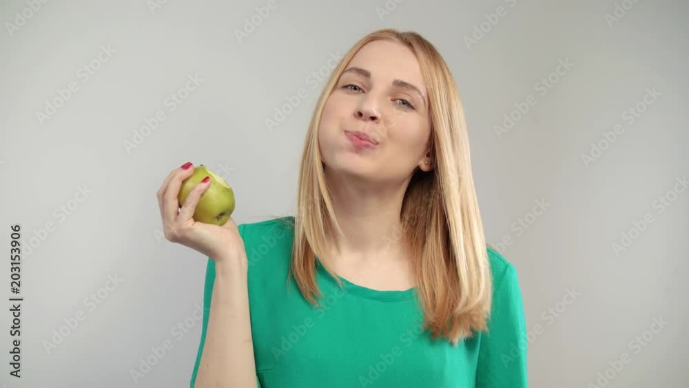 Portrait of blonde woman eating green apple at white background. Blonde girl biting natural fruit at studio. Close up of young woman propose to bite organic apple Portrait of blonde woman eating green apple at white background. Blonde girl biting natural fruit at studio. Close up of young woman propose to bite organic apple