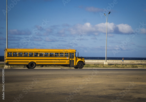 Fotografie photograph of a very old school bus, from the 60s, crossing a highway that is next to the sea