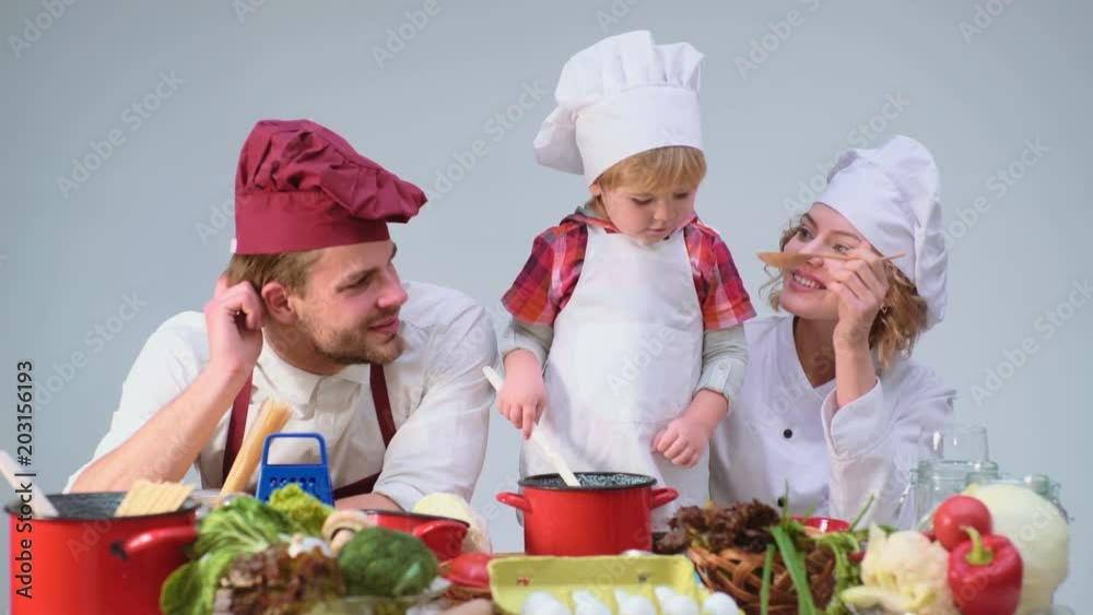 Family cooking kitchen food fogetherness concept. Family cooking meal In kitchen together. Cute little boy and his handsome dad cutting vegetables and smiling while cooking in kitchen at home. Family cooking kitchen food fogetherness concept. Family cooking meal In kitchen together. Cute little boy and his handsome dad cutting vegetables and smiling while cooking in kitchen at home.