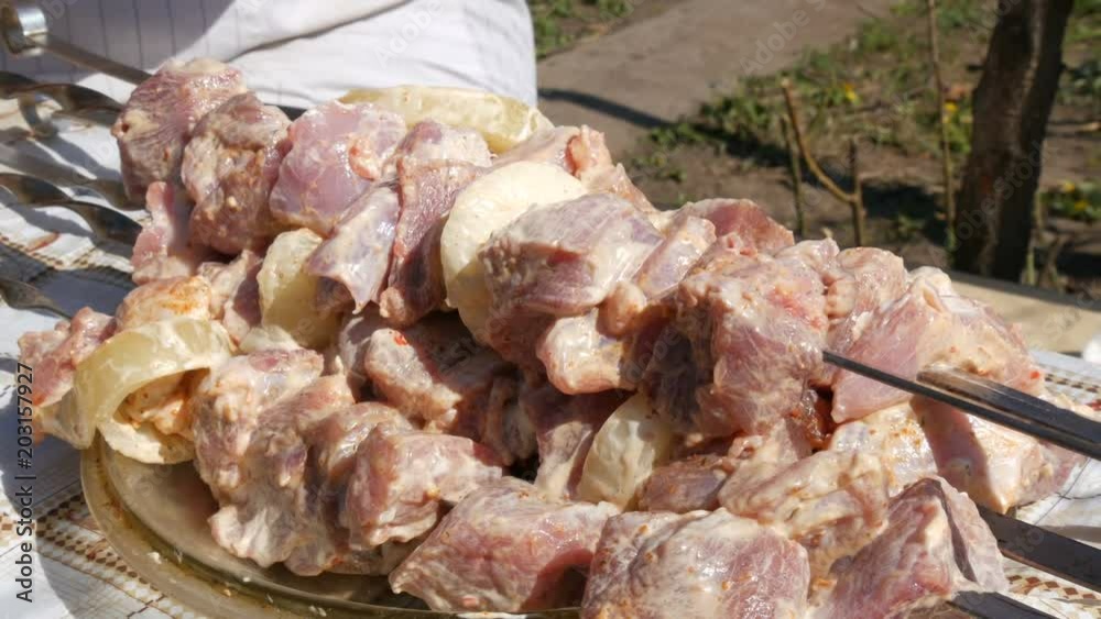 Large pieces of fresh pickled meat on skewers ready for a barbecue. A man takes and puts raw meat on a skewer Large pieces of fresh pickled meat on skewers ready for a barbecue. A man takes and puts raw meat on a skewer