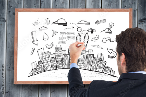 Rear view of businessman writing with a white chalk against blackboard with copy space on wooden board