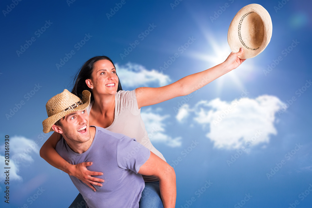 Fototapeta premium Man giving his pretty girlfriend a piggy back against bright blue sky with clouds