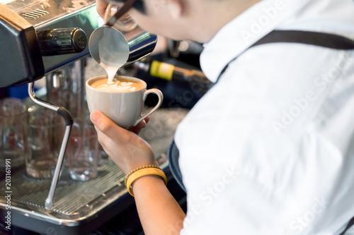 Close up of Asian barista holding a white cup making a latte art coffee in Coffee Shop. Preparation Service Concept