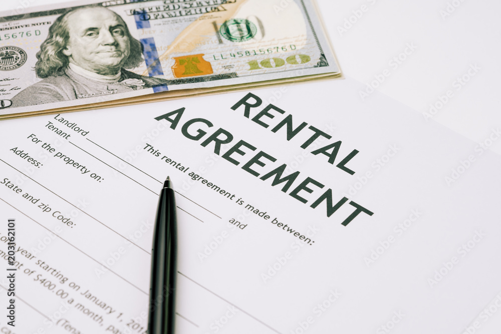 Pen and US Dollar banknotes money on rental agreement form document, ready to sign contract, property or real estate deal between landlord and tenant concept