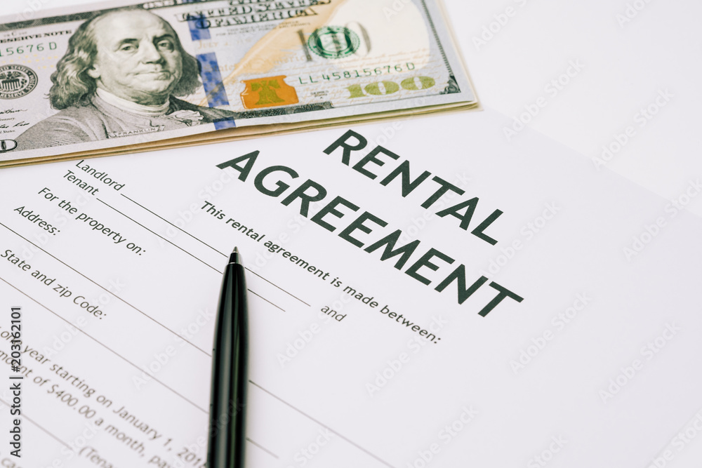 Pen and US Dollar banknotes money on rental agreement form document, ready to sign contract, property or real estate deal between landlord and tenant concept Pen and US Dollar banknotes money on rental agreement form document, ready to sign contract, property or real estate deal between landlord and tenant concept