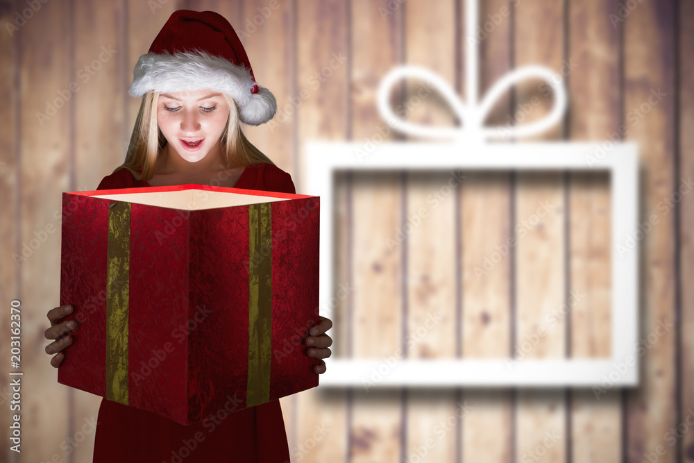 Festive blonde holding a gift against blurred christmas decorations on wood
