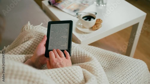 CloseUp to Ebook Reader in Hands of Adult Woman Sitting in a Cozy Room at Home with Coffee Cup