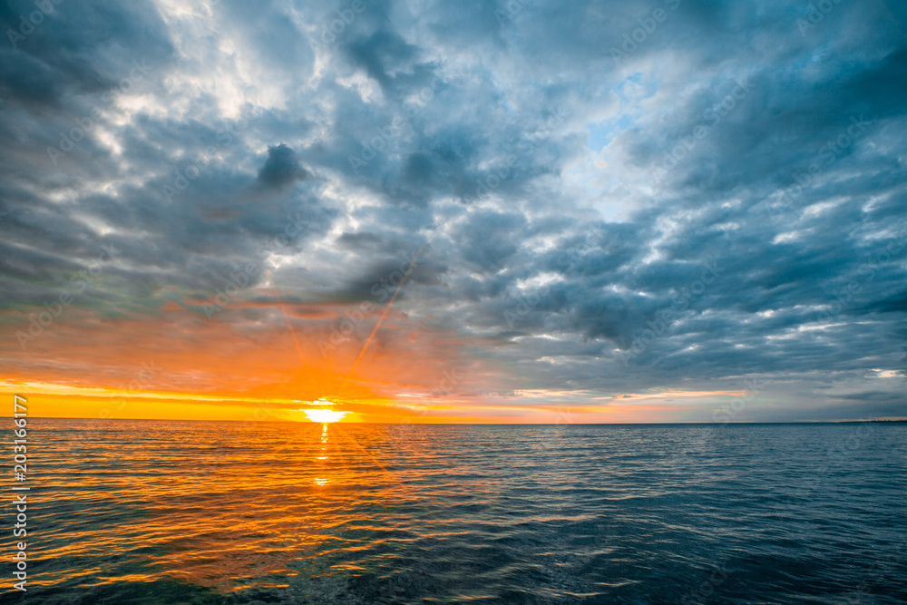 Minimalist seascape - stormy clouds over calm waters with sun touching the horizon