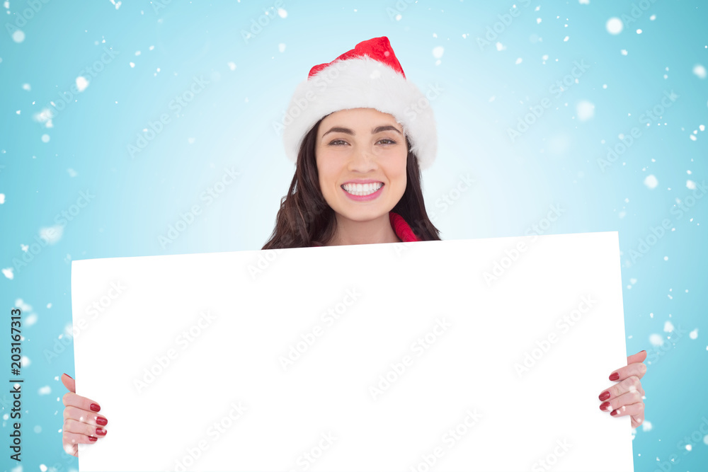 Smiling brunette in santa hat showing white poster against blue vignette Smiling brunette in santa hat showing white poster against blue vignette
