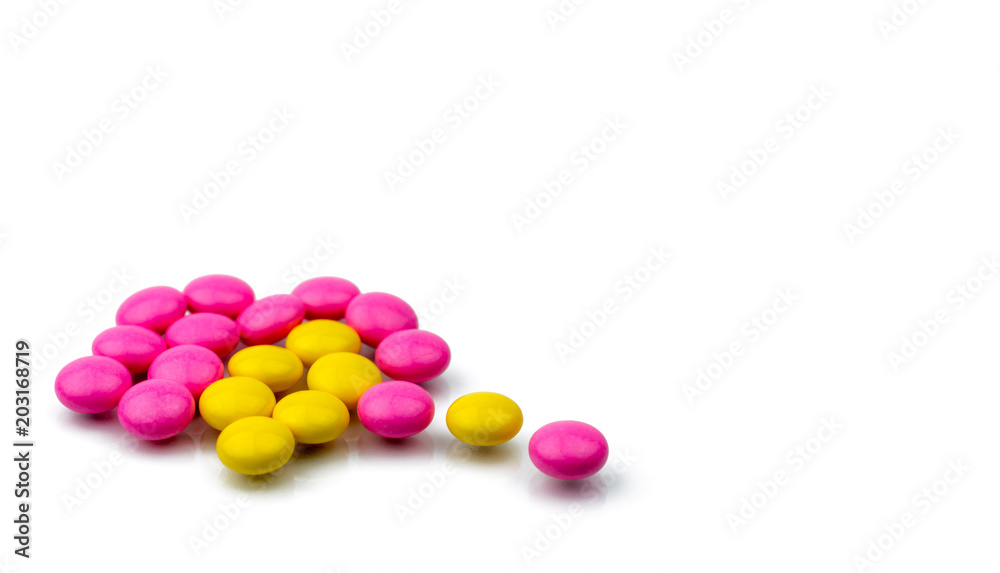 Pile of pink and yellow round sugar coated tablets pills isolated on white background with copy space. Colorful pills for treatment anti-anxiety, antidepressant and migraine headache prophylaxis. Pile of pink and yellow round sugar coated tablets pills isolated on white background with copy space. Colorful pills for treatment anti-anxiety, antidepressant and migraine headache prophylaxis.