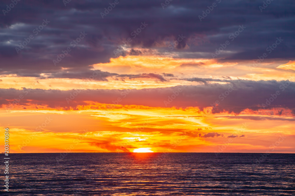 Tranquil vivid sunset with glowing orange clouds and calm ocean water