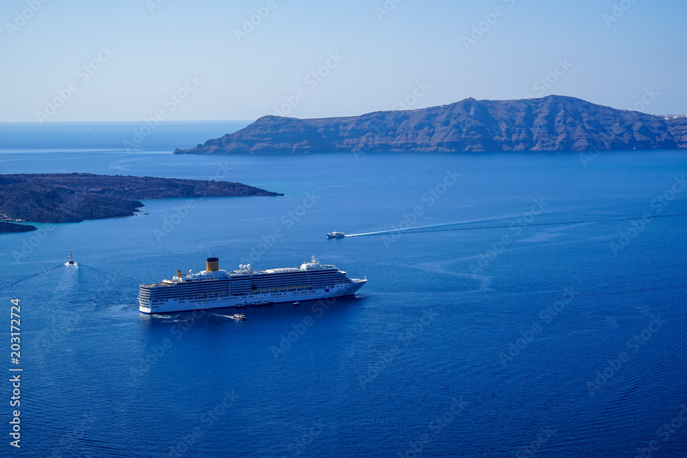 Large ferry ship and speed boats sailing on vast blue mediterranean sea with caldera mountain and sky background, Santorini