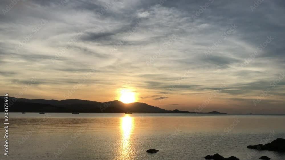 Dramatic beautiful sunset at beach awesome sun golden reflection on calm waves surface and mountain background. Tranquil idyllic scene of a summer sunset over the sea, waves slowly splashing on coast.