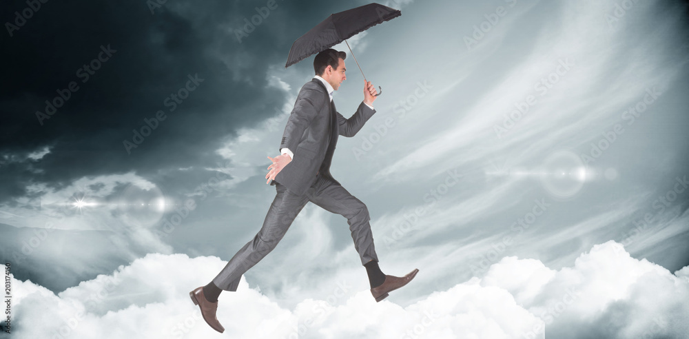 Businessman jumping holding an umbrella against blue sky