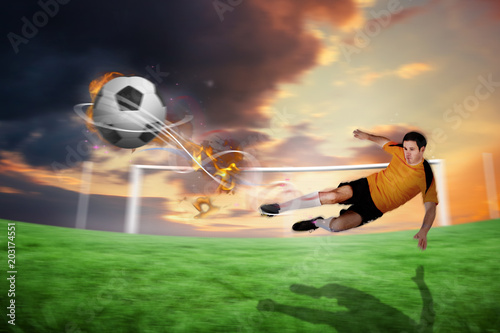 Football player in orange kicking against football pitch under cloudy orange sky © vectorfusionart