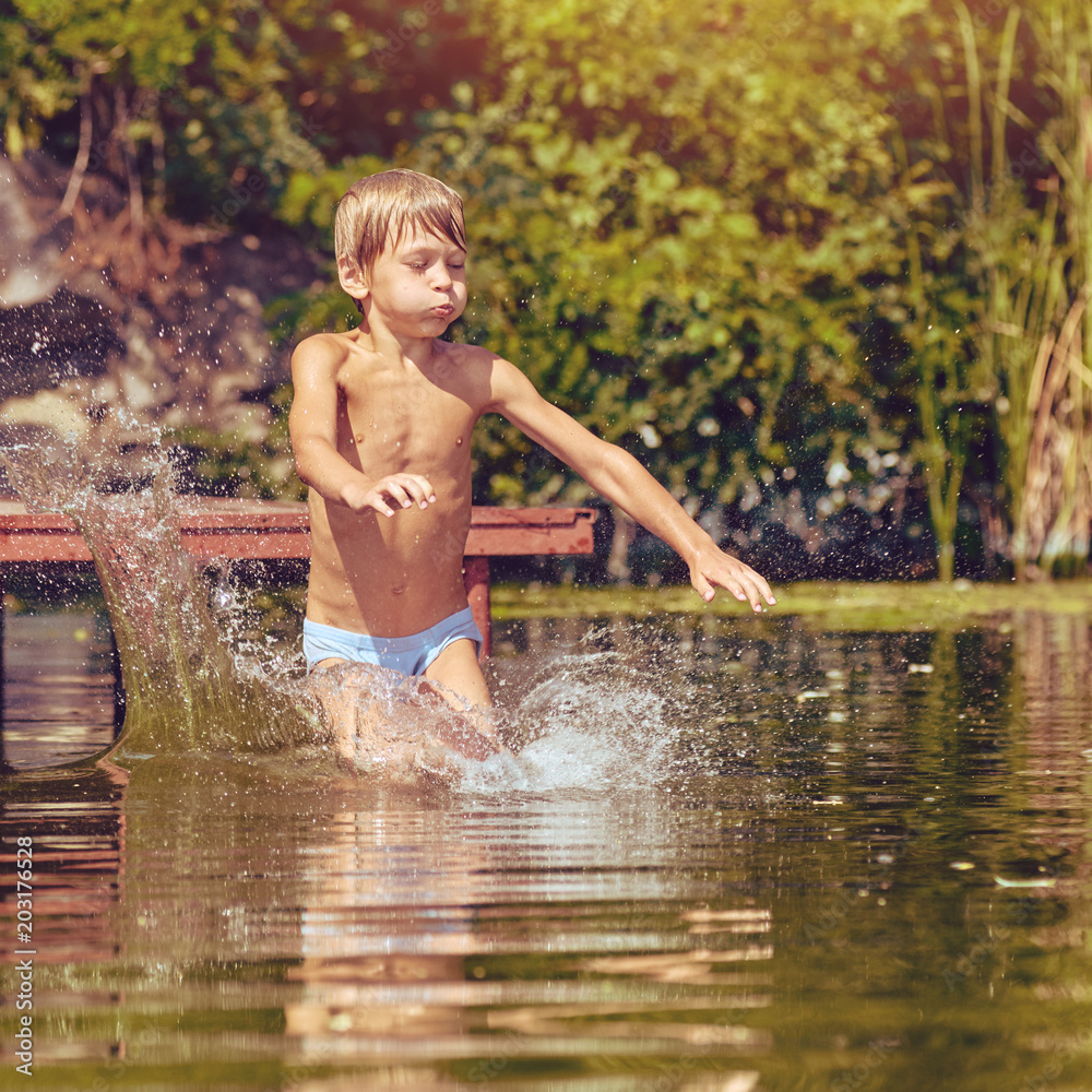 Fototapeta premium Little boy having fun and jumping into the river from pier, image with square aspect ratio and warm toning