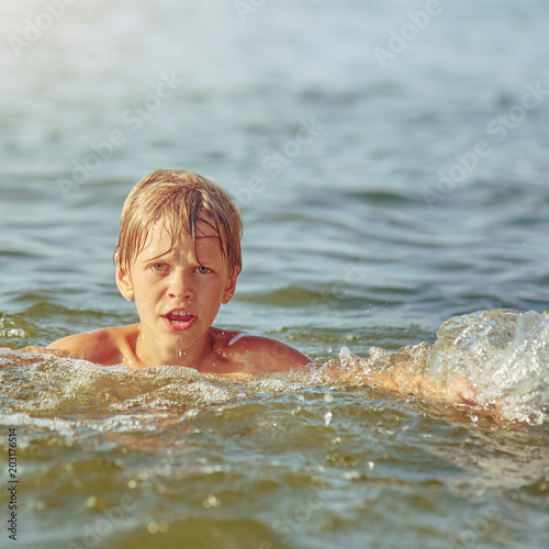 Happy little boy swimming in the river on summer weekend, image with square aspect ratio and warm toning © Denys Kurbatov