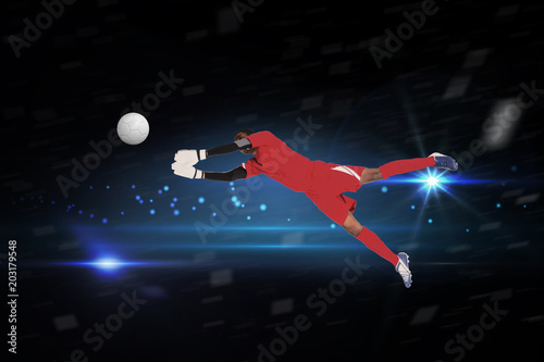 Goalkeeper in red making a save against black background with spark