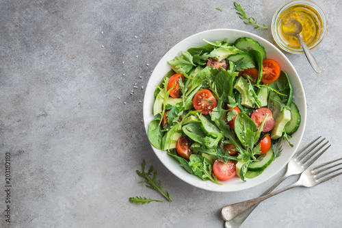 healthy vegan salad (tomatoes, avocado, cucumber, spinach and arugula) in white bowl