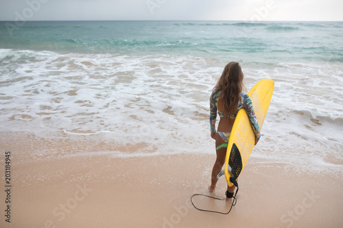 Girl surfer holds a board and goes into the ocean.