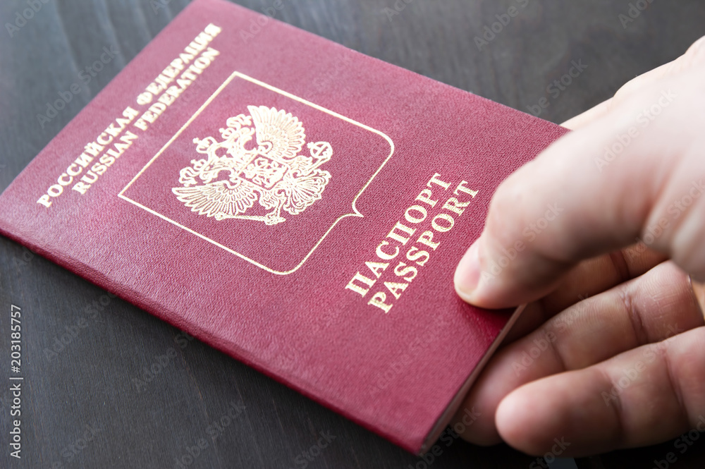 Male hand holding red passport. Grey wood background Male hand holding red passport. Grey wood background