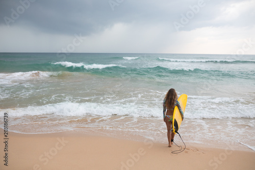 Girl surfer holds a board and goes into the ocean.