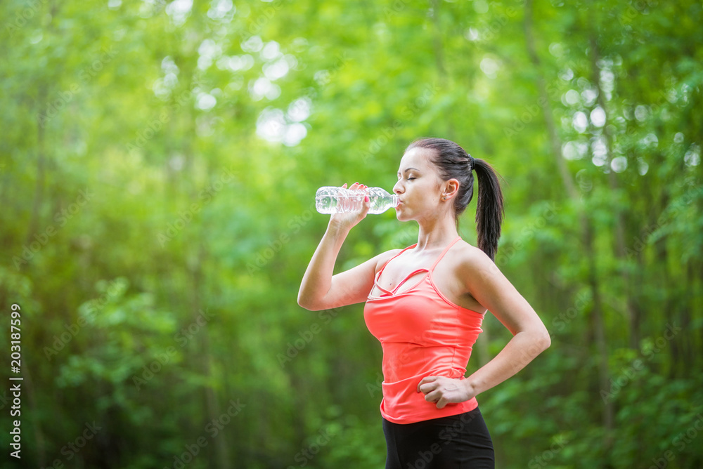 Young attractive woman drinking bottled water in the park after training/doing exercises. Healthy lifestyle concept. Young attractive woman drinking bottled water in the park after training/doing exercises. Healthy lifestyle concept.