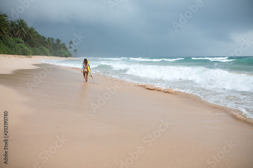 Back view of a attractive woman holding surf board in hands on coastline.
