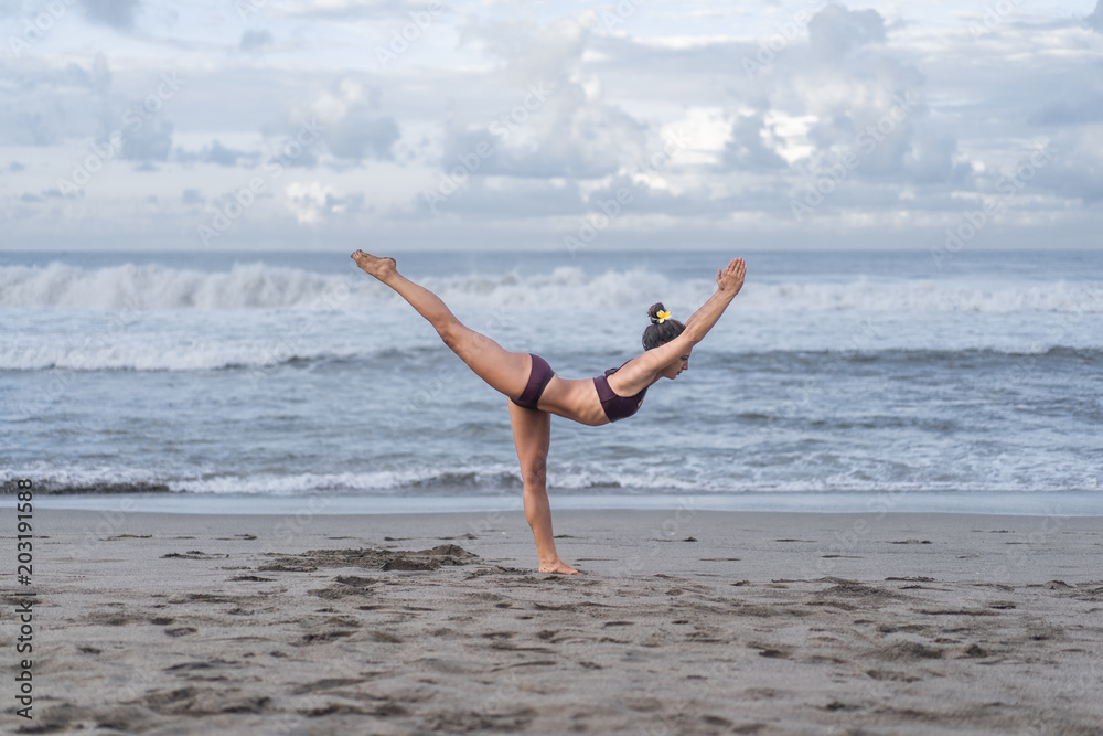 side view of young woman practicing yoga in Warrior III pose (Virabhadrasana III) on seashore