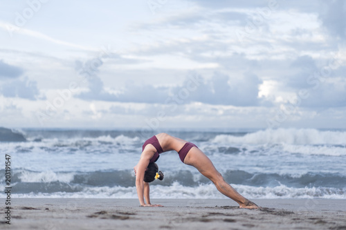 side view of young woman practicing yoga in Wheel pose (Urdhva Dhanurasana) on seashore