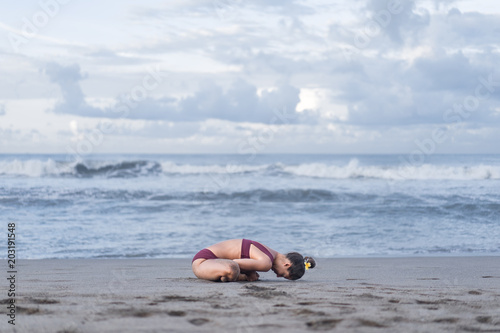 side view of young woman practicing yoga and preparing for Scale pose (Tolasana) on seashore photo