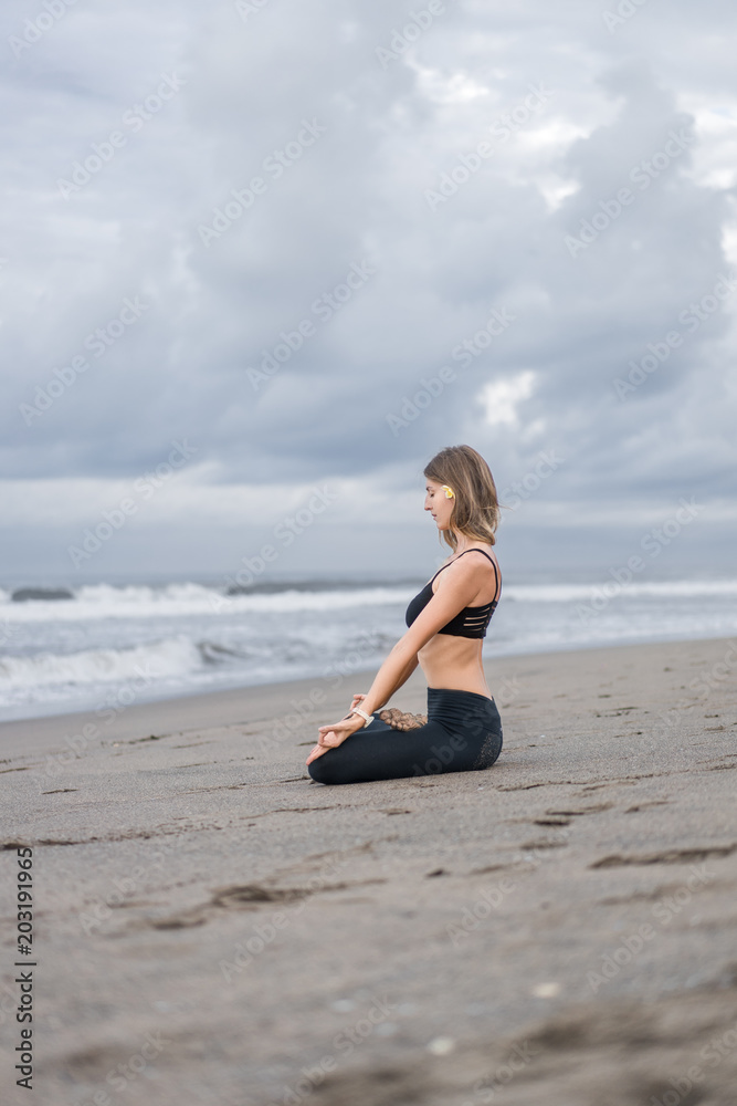 side view of beautiful young woman practicing yoga in lotus pose and meditating on seashore