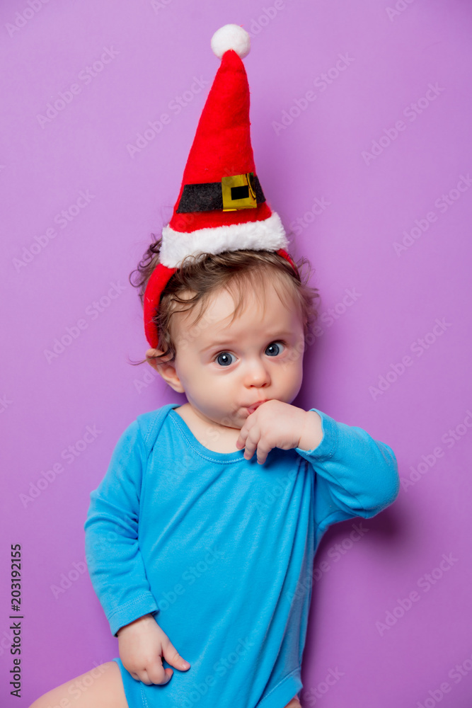 Little infant baby in Christmas hat on purple background Little infant baby in Christmas hat on purple background