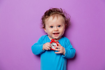 little infant baby with alarm clock lying on purple background