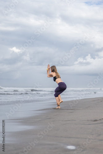 sporty young woman practicing yoga in Eagle pose (Garudasana) on seashore