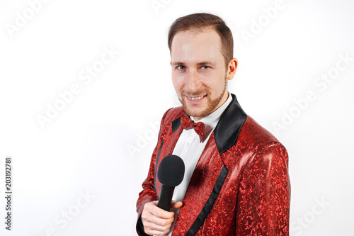 A young man with a microphone on a white background in a red jacket, leading with a microphone